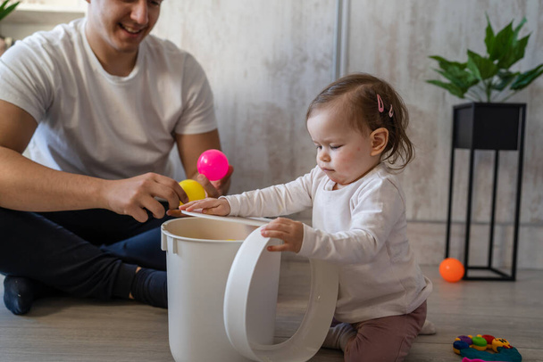 baby girl and her father young caucasian man with daughter playing at home happy sitting on the floor with toys in day fatherhood childhood family concept real people copy space - Foto, Imagem