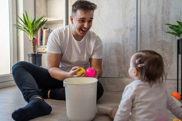 csecsemő lány és az apja fiatal kaukázusi férfi lánya játszik otthon boldog ül a padlón játékokkal nappal apaság gyermekkor családi koncepció valós emberek másolja tér - Fotó, kép
