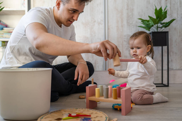 dítě dívka a její otec mladý běloch muž s dcerou hrát doma šťastný sedí na podlaze s hračkami v den otcovství dětství rodinný koncept skuteční lidé kopírovat prostor - Fotografie, Obrázek