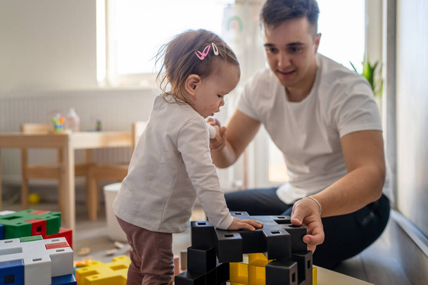 baby girl and her father young caucasian man with daughter playing at home happy sitting on the floor with toys in day fatherhood childhood family concept real people copy space - Fotó, kép