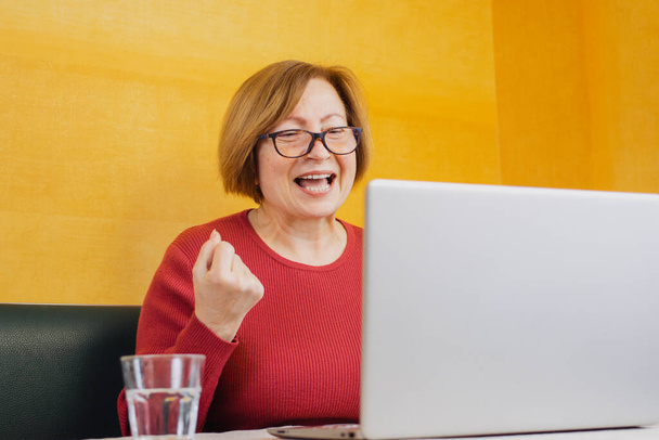 Excited elderly woman look at computer screen triumph win lottery online. Feeling euphoric read good promotion news or sale offer, celebrate success victory, new opportunity, got new job, great result - Photo, Image