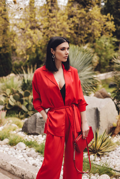 fashion outdoor photo of beautiful woman with dark hair in elegant red suit posing in summer park - Fotoğraf, Görsel