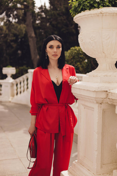 fashion outdoor photo of beautiful woman with dark hair in elegant red suit posing in summer park - Photo, Image
