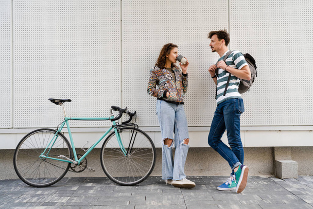 man and woman young couple posing in front of white wall of modern building in day students or tourists caucasian male with mustaches boyfriend and girlfriend happy smile talking to each other - Photo, Image