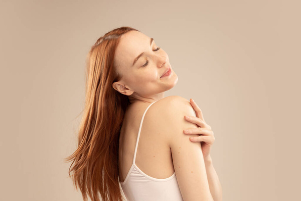 Portrait of beautiful young red-haired girl smiling, posing isolated over grey studio background. Looks delightful. Concept of natural beauty, body and skin care, health, spa, wellness, cosmetics, ad - Foto, Imagem