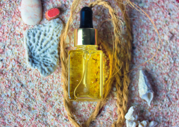 Yellow oil serum essence in glass bottle flatly. Concept of natural cosmetic, trendy beauty skin care. Sunscreen oil to protect the face body at summer days. Sea theme, seashells, stones, pink sand.  - Foto, Imagem