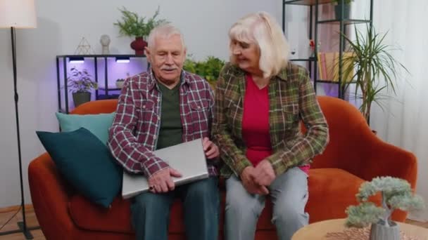 Старшие пожилые семьи пара бабушки и дедушки мужчина женщина сидит на диване в домашней комнате и открывает ноутбук. Пожилая бабушка дедушка начинает работать за компьютером, отправляет сообщения, делает онлайн покупки - Кадры, видео