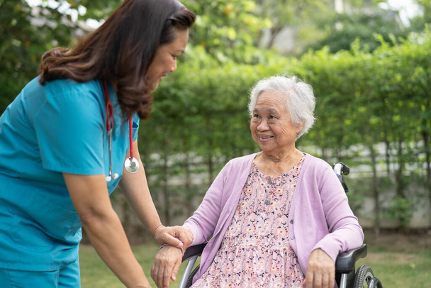 Doctor caregiver help and care Asian senior or elderly old lady woman patient sitting on wheelchair in park at nursing hospital, healthy strong medical concept - Photo, image