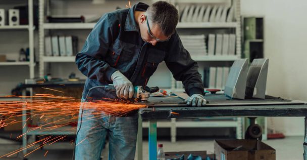 Heavy Industry Engineering Factory Interior with Industrial Worker Using Angle Grinder and Cutting a Metal Tube. Contractor in Safety Uniform and Hard Hat Manufacturing Metal Structures. High-quality - Фото, зображення