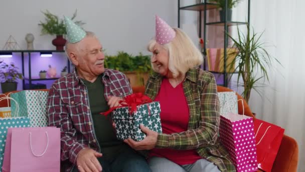 Iloinen vanhempi vanhempi perhe pari isovanhemmat mies nainen juhlii syntymäpäivää sohvalla kotona. Kypsä isoäiti vaimo antaa lahja laatikko yllätys lahja miehelleen isoisä - Materiaali, video