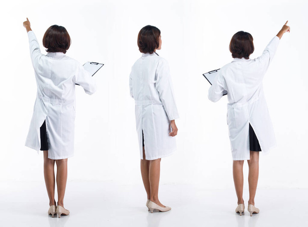 Pleine longueur 20s jeune asiatique médecin femme porter stéthoscope ; manteau uniforme, pointant la main du doigt dans l'air. Hôpital femelle transporter patient dossier données heureux sourire sur fond blanc isolé - Photo, image