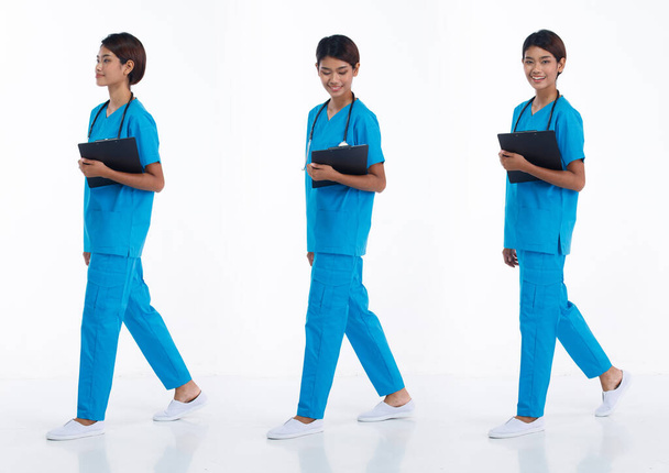Full length 20s young Asian Nurse Woman wear stethoscope; blue uniform, walking forward right left. Hospital female carry patient chart data happy smile over white background isolated - Photo, Image