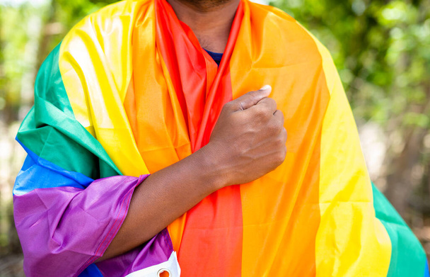 homem orando abraçando a bandeira do orgulho lgbtq abraçando durante a marcha do orgulho conceito de liberdade e individualidade - Foto, Imagem