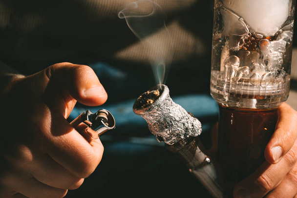 Zbliżenie człowieka palącego trawkę, medyczną marihuanę lub marihuanę z bonga lub rury wodnej. Koncepcja legalizacji marihuany i trawki. Wysokiej jakości zdjęcie - Zdjęcie, obraz