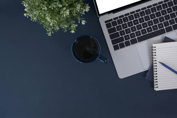 Stylowy obszar roboczy z laptopem, notebookiem i filiżanką kawy na ciemnoniebieskim tle. Widok z góry, płaski. - Zdjęcie, obraz