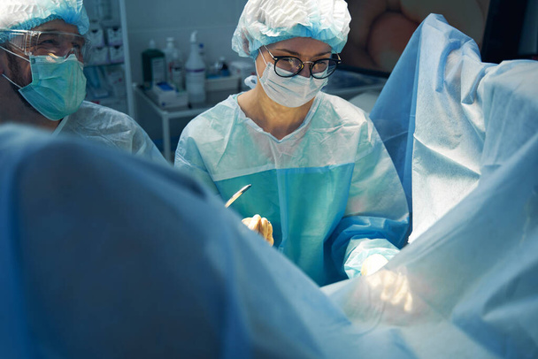 男性アシスタントから腹腔鏡機器を取得しながら手術領域を見て女性外科医 - 写真・画像