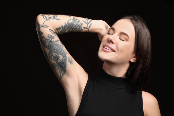 Beautiful woman with tattoos on arm against black background - Zdjęcie, obraz