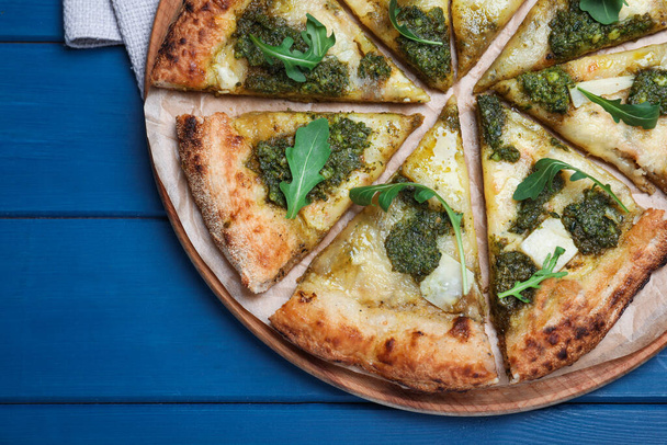 Delicious pizza with pesto, cheese and arugula on blue wooden table, top view - Foto, afbeelding