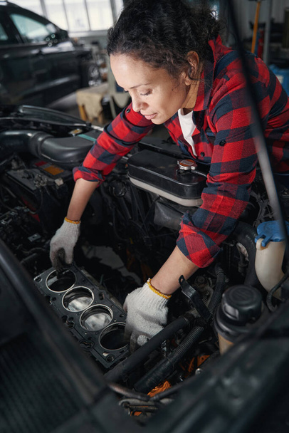Female vehicle technician in work gloves repairing automobile engine in car repair garage - Foto, Imagen
