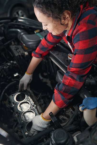Woman vehicle technician in work gloves repairing automobile motor in car repair garage - Foto, Bild