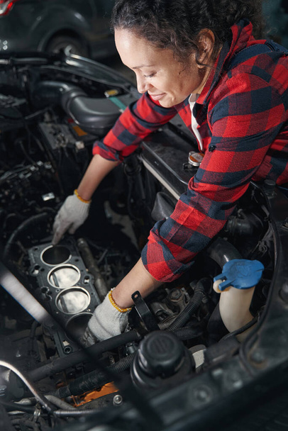 Female vehicle technician in work gloves fixing automobile motor in car repair garage - 写真・画像