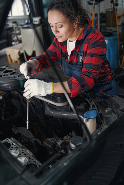 Woman vehicle technician using torque wrench tool while fixing car engine in auto repair shop - 写真・画像