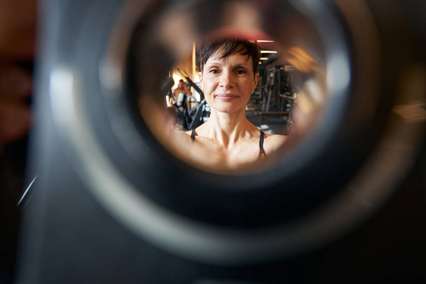 Portrait of professional female athlete looking through hole in barbell weight plate - Valokuva, kuva