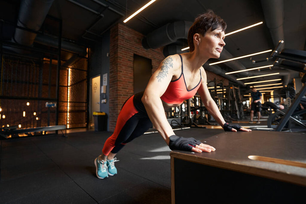 Strong muscular female athlete performing push-ups on plyometric box during gym workout - Fotó, kép