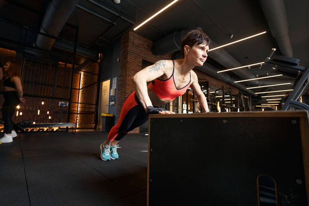 Strong brawny woman doing press-up exercise on plyometric box in fitness studio - Foto, afbeelding