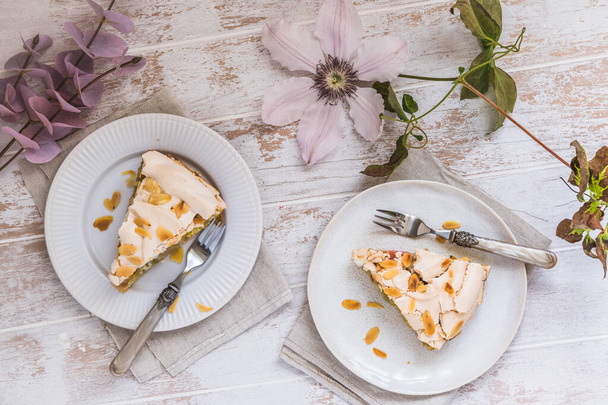 Pieces of rhubarb pie with meringue topping and almonds on white wooden background, top view - 写真・画像