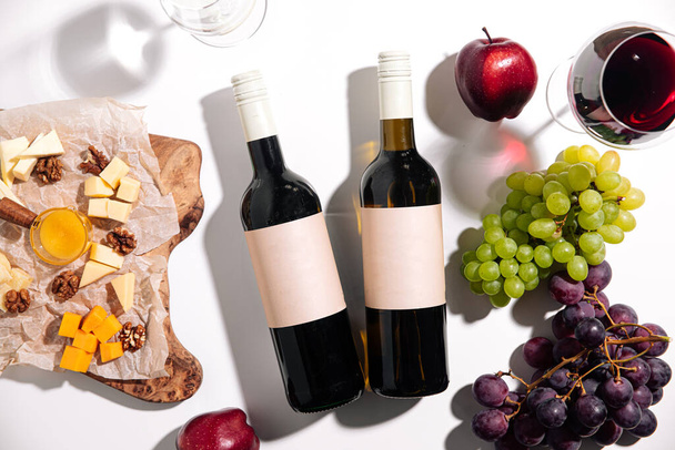 Vista superior de botellas de vino con aperitivos sobre fondo blanco - Foto, Imagen