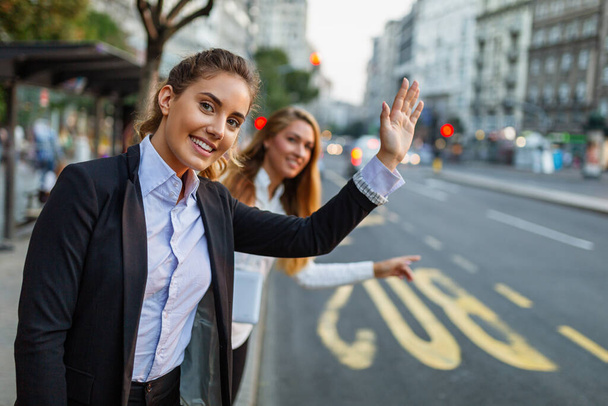 Businesswomen waving for a cab in city next to road - Foto, Imagem
