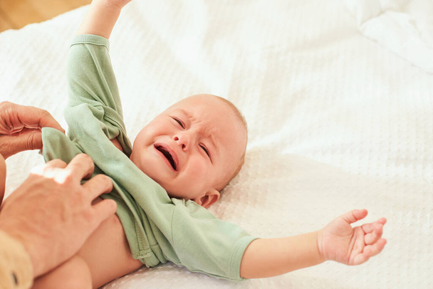 Płaczące niemowlę w piżamie na śnieżnobiałym łóżku. Dziecko i opieka. Opieka zdrowotna, dziecięcy sen, zmiana pieluch. Koncepcja dzieciństwa. - Zdjęcie, obraz