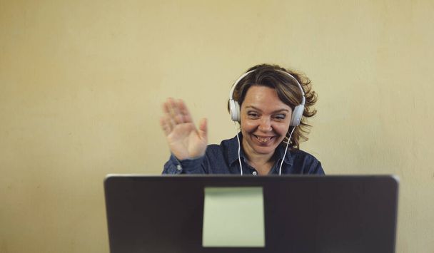 Fröhliche vierzigjährige Frau, die sich per Laptop online unterhält. Porträt einer blonden Frau im blauen Jeanshemd - Foto, Bild