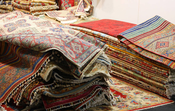 pila de muchas alfombras persas de lana con diseños geométricos de colores para la venta en tienda especializada en muebles para el hogar - Foto, Imagen