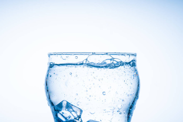 A jégkocka beleesett a pohár vízbe. Víz fröccsent a tiszta pohárból. Új koncepció - Fotó, kép