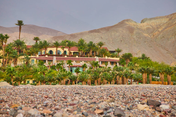 Imagem de planícies e montanhas do deserto rodeiam um deslumbrante oásis de hotel repleto de palmeiras - Foto, Imagem