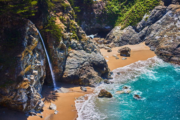 海の入り江の隣の砂浜に滝が放出される海岸岩のイメージ - 写真・画像