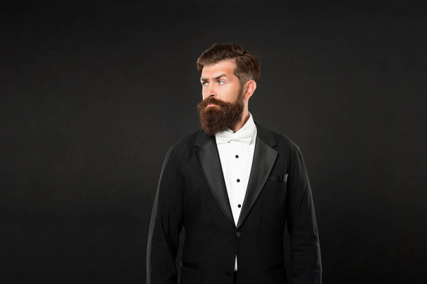 serious man in tuxedo bow tie looking aside. bride groom in formalwear on black background. male formal fashion. - Photo, Image