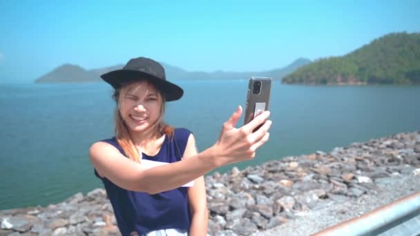 aziatische vrouw is het nemen van selfie met behulp van mobiele telefoon op een strand kant met eiland achtergrond. - Video