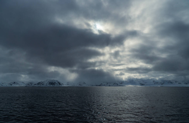 Dramatic arctic mountain landscape in Svalbard. Dramatic clouds over snowy mountains in the arctic. In the foreground the Greenland Sea. High quality photo - Valokuva, kuva