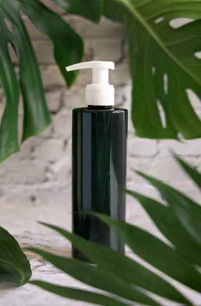 Dark green one pump dispenser and tropical monstera leaves on marble table close up. Brand packaging mockup. Skincare beauty product. Natural herbal cosmetics concep - Foto, Bild