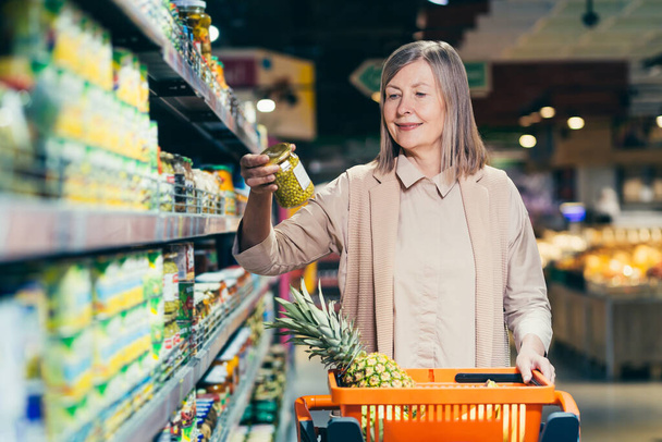 Senior woman in a supermarket chooses groceries in the grocery department - Foto, Imagen