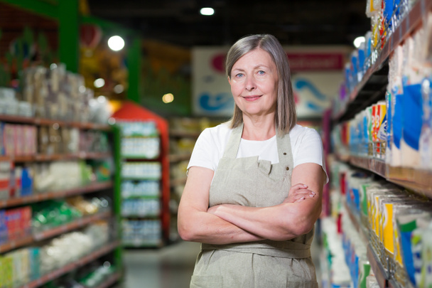 Portrait of happy senior woman grocery store employee with arms crossed smiling and looking at camera - Fotó, kép