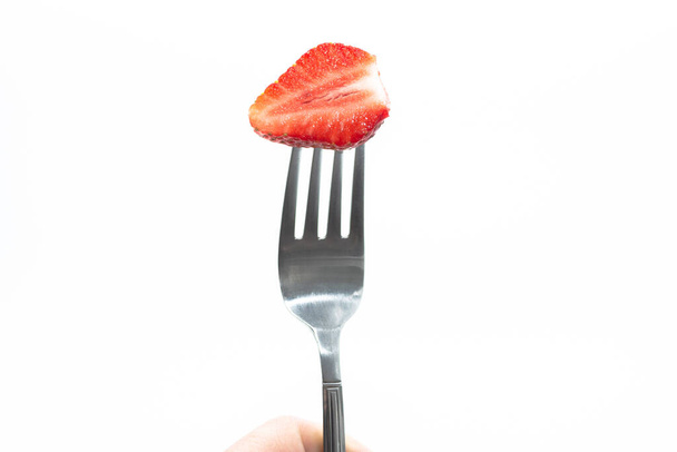 Polovina zralé šťavnaté červené jahody na kovové vidličce na bílém pozadí. - Fotografie, Obrázek