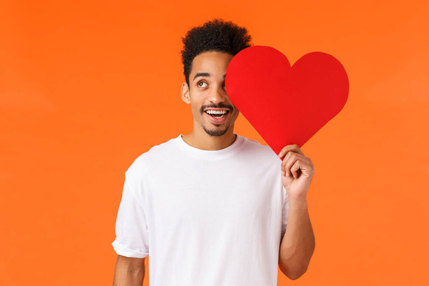 Dreamy handsome african-american guy found true love, giving valentines card to lover, looking upbeat up thoughtful, imaging perfect date, express own love and affection, standing orange background. - Photo, Image