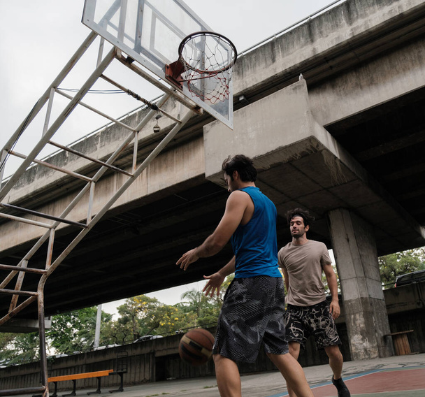 Két kaukázusi férfi kosárlabdázik a bíróságon a városi utcában.. - Fotó, kép