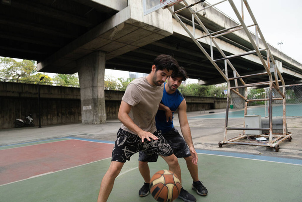 Zwei kaukasische Männer praktizieren Baskegball vor Gericht an der Stadtstraße. - Foto, Bild