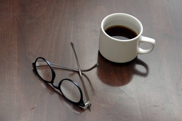 Полуполная чашка кофе и очки на деревянном столе - Фото, изображение