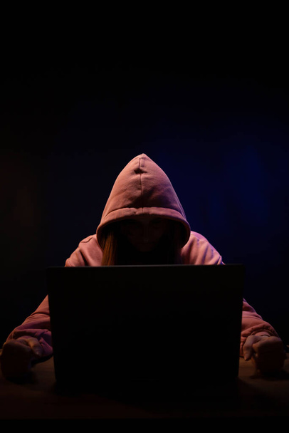 Хакер рядом с ноутбуком. Женщина-хакер на фоне темной комнаты - Фото, изображение